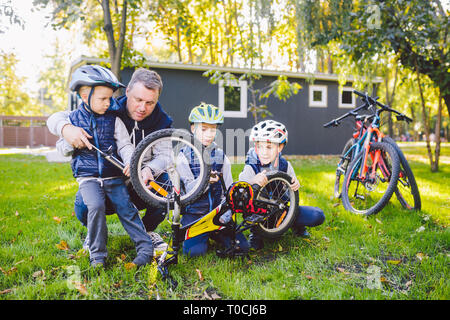 Father's day A big friendly family father and three sons joint active rest outside. Dad teaches sons to repair cycling. The child uses the pump tool