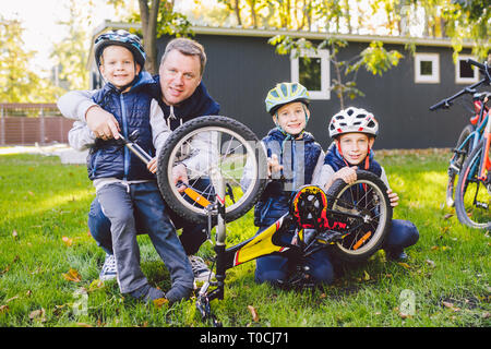 Father's day A big friendly family father and three sons joint active rest outside. Dad teaches sons to repair cycling. The child uses the pump tool