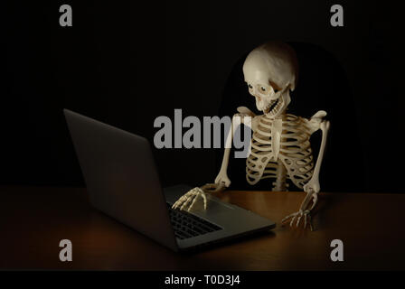 skeleton with skull working on laptop at night with amazement on his face Stock Photo