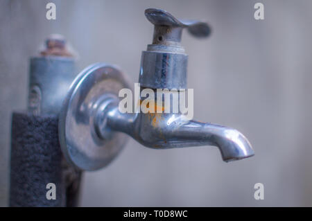 A rusted tap with no water against a grey background Stock Photo