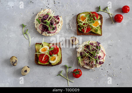 Healthy sandwiches with avocado, tomato, quail eggs, radishes and micro greens (sprouts) on a dark background, flatlay Stock Photo