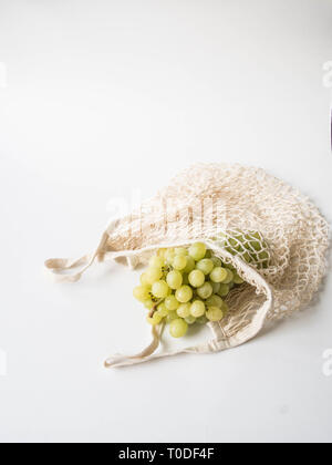 Eco-friendly beige shopping bag with grapes on a white background. String bag with fruits. Zero waste, no plastic concept. Copy space Stock Photo