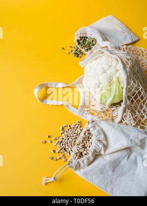 Eco-friendly beige shopping bags with cauliflower, beans, pumpkin seeds on yellow background. String bag with vegetables. Zero waste, no plastic conce Stock Photo