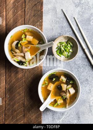Japanese miso soup with oyster mushrooms in a white bowls with a spoon and white chopsticks on a grey and wood backgrounds. Stock Photo