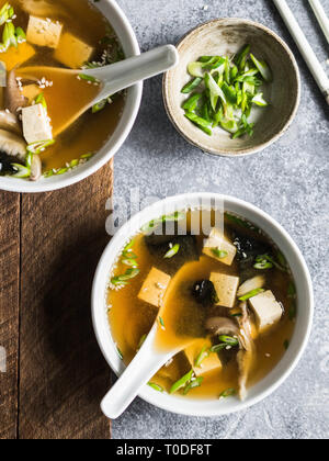 Japanese miso soup with oyster mushrooms in a white bowls with a spoon and white chopsticks on a grey and wood backgrounds. Top view Stock Photo