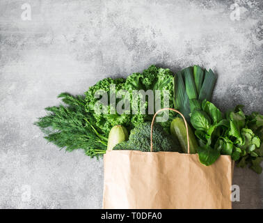 Healthy green vegan ingredients for cooking. Various clean green vegetables and herbs in paper bag on grey background. Products from the market withou Stock Photo