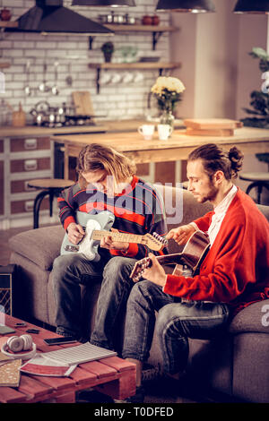 Participants of band sitting on sofa and playing music instruments Stock Photo