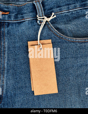 tied on a rope is an empty rectangular brown paper tag on blue jeans, full frame Stock Photo