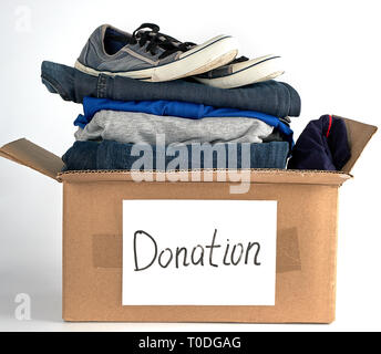 folded clothes and shoes in a brown paper box with the inscription donation on a white background, the concept of helping people in need Stock Photo