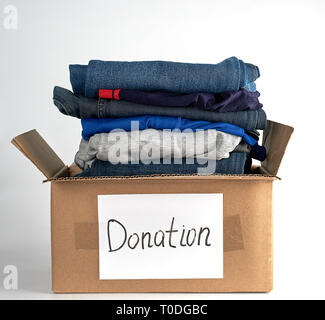 folded clothes in a brown paper box with the inscription donation  on a white background, the concept of helping people in need Stock Photo