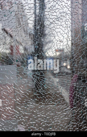 Close-up of a broken and shattered glass pane or window, blurred city view in the background. Stock Photo