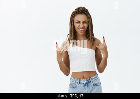 Woman thinks expressing yourself is awesome. Portrait of beautiful and stylish dark-skinned girl with dreads wrinkling nose showing rock n roll sign Stock Photo