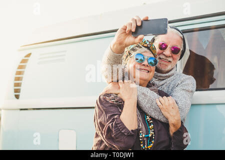 70 years old cheerful happy adult couple take a selfie picture outside a intage blue van with modern technologyh - tourism and tourist concept for peo Stock Photo