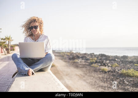 Technology and travel. Working outdoors. Freelance concept. Pretty young woman using laptop  beach. Stock Photo
