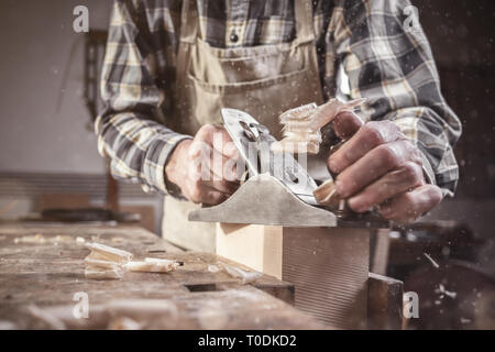 Arms and hands of a carpenter working with a planer tool in a dusty workshop Stock Photo