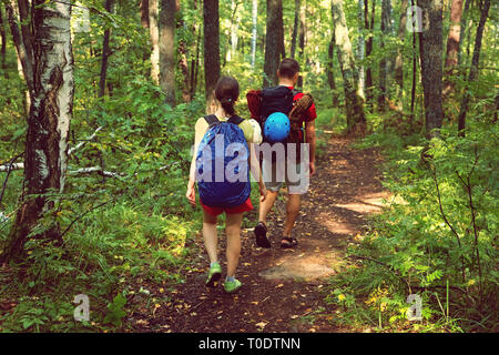 Young couple hikers in forest. sports man and woman with backpacks on road in nature Stock Photo