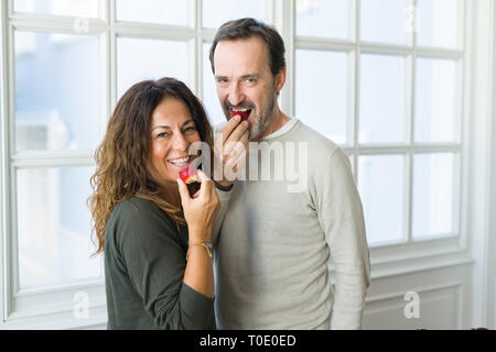 Middle age senior couple eating a fresh strawberry at home Stock Photo