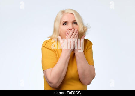 Old lady wearing yellow clothes, covering her mouth with palms. Stock Photo