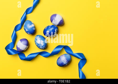 Multicolored Easter eggs with blue ribbon on yellow background. Blue, purple and violet boiled chicken eggs with blue ribbon. Concept of Easter banner Stock Photo