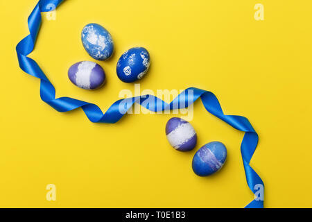 Multicolored Easter eggs with blue ribbon on yellow background. Blue, purple and violet boiled chicken eggs with blue ribbon. Concept of Easter banner Stock Photo