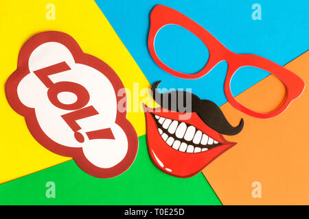 Flat lay of paper props in form of face with lol text in speech bubble on colorful background minimal creative fun concept. Stock Photo