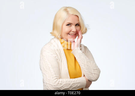 Senior caucasian woman with blonde hair in white and yellow sweater smiling Stock Photo