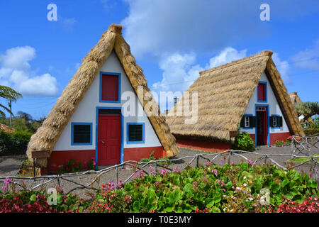 Typical stone houses, painted red, white and blue, with triangular shaped straw thatched roof in the village of Santana / Santa Ana, Madeira, Portugal Stock Photo