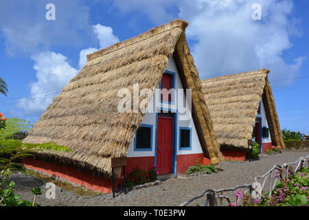 Typical stone houses, painted red, white and blue, with triangular shaped straw thatched roof in the village of Santana / Santa Ana, Madeira, Portugal Stock Photo