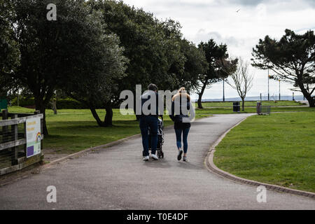 Young couple pushing child through the park in a pushchair,  the father is pushing the stroller Stock Photo