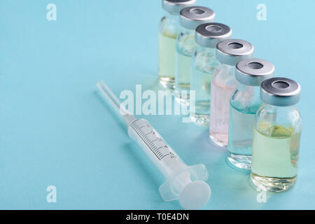 Syringe and vials of different medications on blue background. Protection from viral diseases, pharmacy and healthcare. Stock Photo