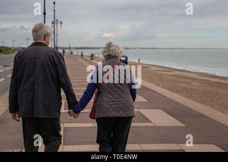 Elderly couple walking along the promenade at the beach holding hands Stock Photo