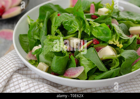 Fresh salad with spinach, pomegranate, cheese, red radish on the table.Close up,  diet food. Stock Photo