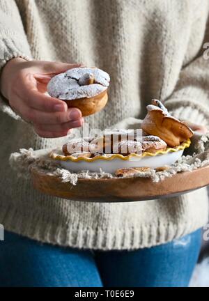 A woman in a sweater holding muffins with icing sugar in her hands. Cozy photo in the style of life. Homemade pastries on wooden bells. Free space for Stock Photo