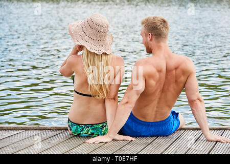 Young couple on summer vacation sits on a jetty at the lake and enjoys nature Stock Photo