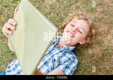 Happy boy using his tablet computer online in nature on a meadow Stock Photo