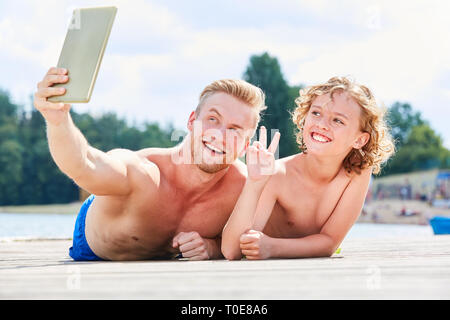 Father and son using tablet computer take a selfie by the sea on summer vacation