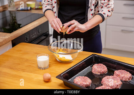 Closeup photo of woman breaking egg in glass bowl. Home cookimg of the meat dish Stock Photo