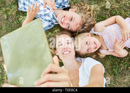Mother and two kids using tablet computer online in nature in summer Stock Photo