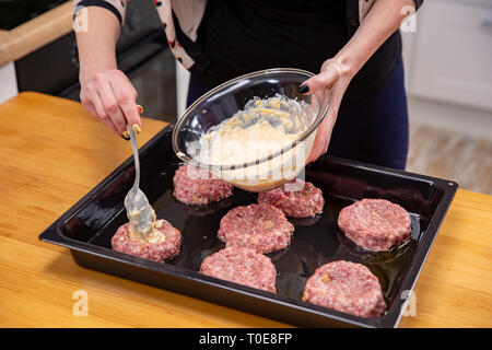 Female hand overlays stuffing theminced meat or meatballs laying on a black baking tray. Process of home cooking. Stock Photo