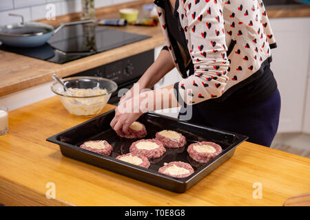 Female hand overlays stuffing theminced meat or meatballs laying on a black baking tray. Process of home cooking. Stock Photo