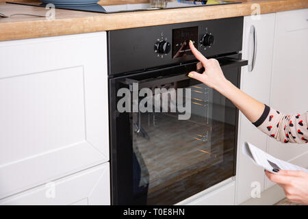 Woman regulating cooking mode on oven panel. A woman is studying the instuction to the new oven Stock Photo