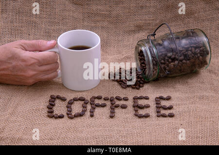 Coffee beans that spell coffee, a coffee mug, and a jar with beans spilled out Stock Photo