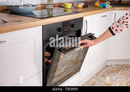 Close up of women hand opening the oven door to control the roast. . Process of home cooking of the meat dish Stock Photo