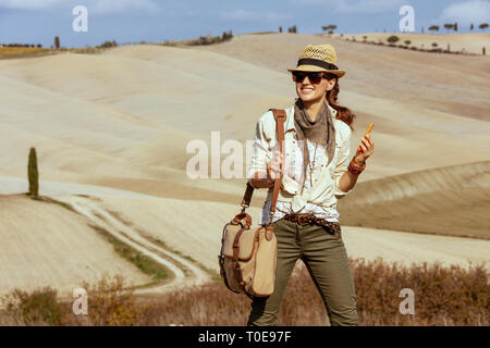 happy healthy solo traveller woman in hiking gear with bag and smartphone using applications while enjoying summer Tuscany view. Stock Photo