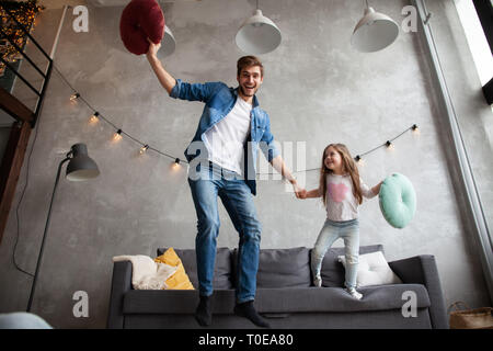 Funny father and cute kid daughter laughing jumping having fun in living room, active family enjoying moving playing with parent at home. Stock Photo