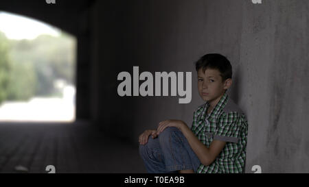 offended abandoned boy sits in a tunnel on the floor, looks at the camera Stock Photo