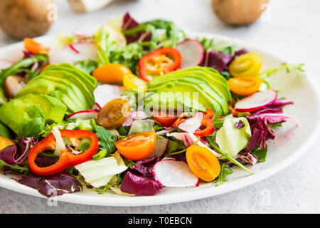 Healthy salad with fresh vegetables, avocado, tomatoes, pepper, radishes, green arugula, onion, spinach and lettuce with olive oil, healthy vegan eati Stock Photo