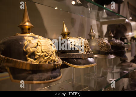 German helmets worn during the First World War on display behind glass display cases in a museum. They are black with brass and a point tip on top. Stock Photo