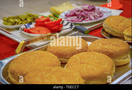 Homemade burger ingredients arranged on tray and plates outdoors. Onion, salted cucumbers, cherry tomatoes, ketchup sauce. Stock Photo