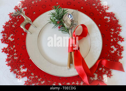 Christmas And New Year Holiday Table Place Setting with branch of Christmas tree and silver deer. Top view, red woolen and white background. Winter holidays concept Stock Photo